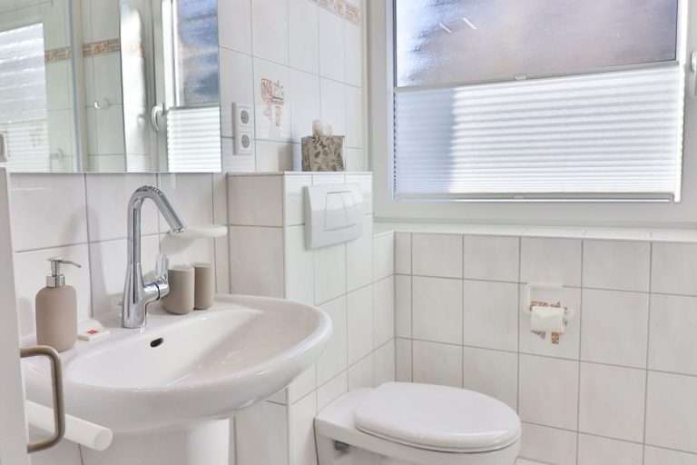 Helles Tageslicht Badezimmer mit Spiegel Toilette, Dusche und Waschbecken. Weiße Fliesen.