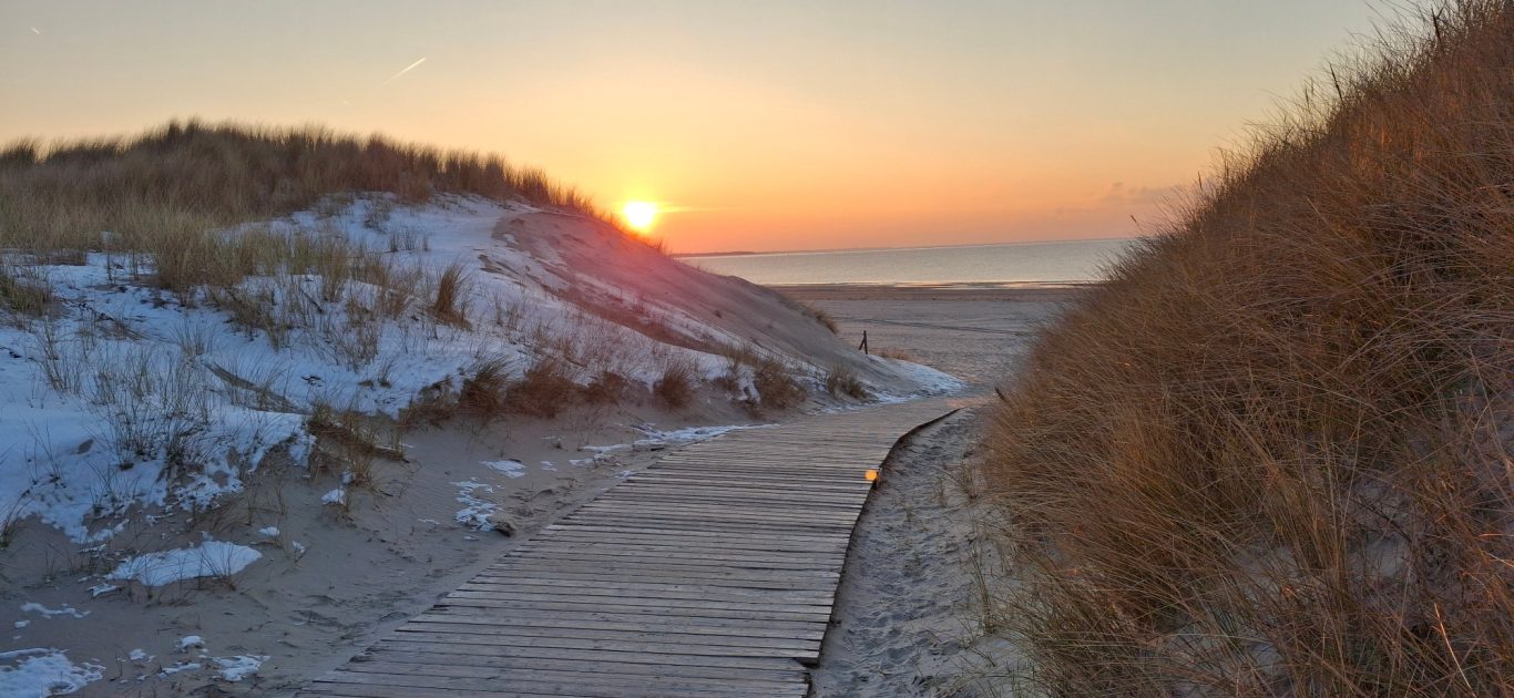 Wintersonne am Strand von Langeoog. Sonnenuntergang am Strand zwischen Dünen und Meer. Es liegt ein bißchen Schnee auf den Dünen.
